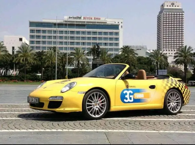 3G Turbo yazılı sarı kaplamalı Porsche kabriyole bir otelin önünde