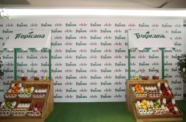 Tropicana logolu zemin panosu önünde ahşap meyve standları